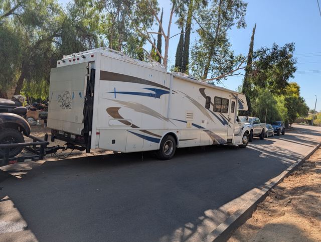 The tribe's RV towing the war car on its trailer, parked along a shady street before departure.