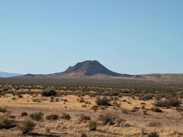A lone volcanic butte rising over flat desert scrubland under a clear sky.