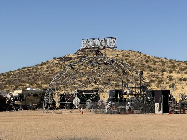 The geodesic Thunderdome frame at the foot of a scrubby hill, a sign on the summit.