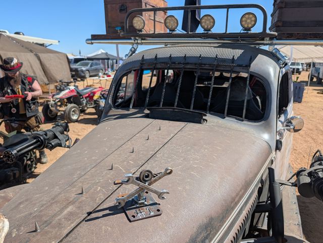 The war car's hood with a crossed-wrench emblem and welded spikes, a roof rack of lights above.