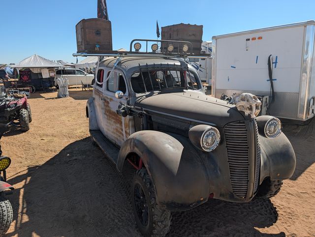 Three-quarter view of the war car with oversized tires, roof crates and a lightbar.