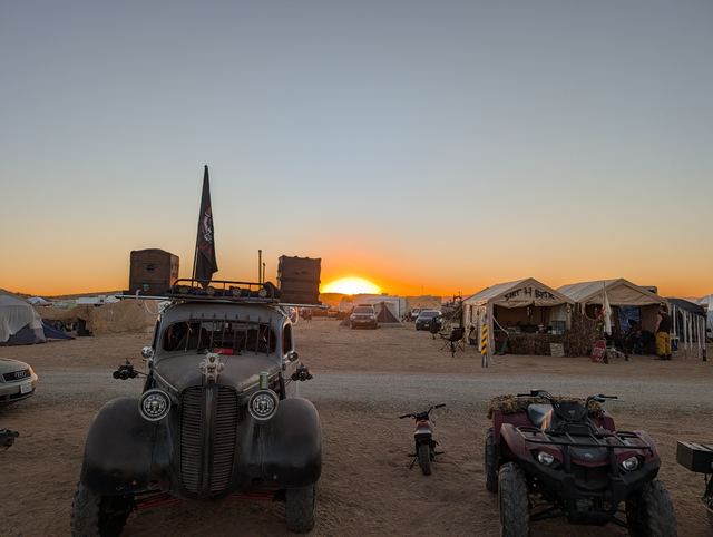 The war car at sunset beside a quad, the sun setting behind camp tents.
