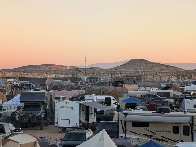 A pink sky over a packed campground and distant hills.