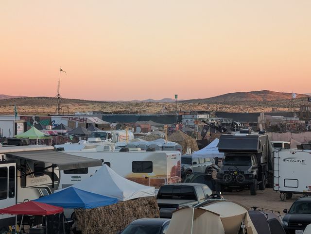 Crowded campground under a fading pink sky, flags poking above the tents.