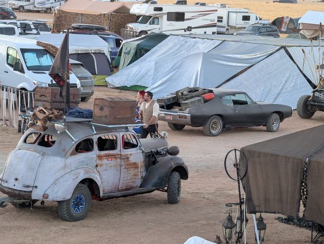 The war car parked among tents and trailers, a few people talking beside it.