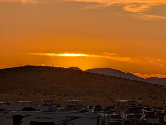 An orange sky over dark hills at sunset above parked campers.