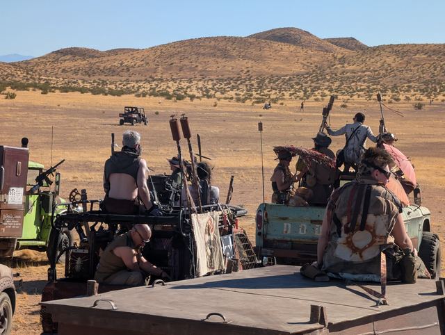 Wastelanders with oars and axes ride on the back of a battered truck.