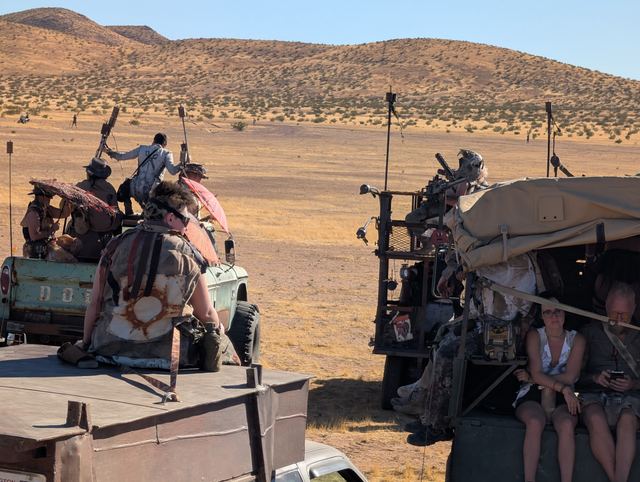 Riders in armor and furs crowd the back of a war rig, axes raised.