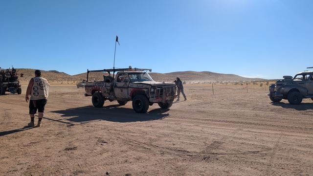 A painted pickup driving across the flats, a wastelander walking alongside.