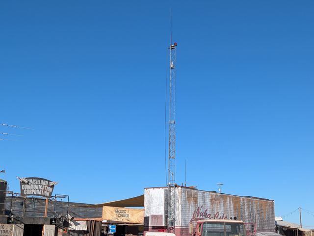 The radio tower rising over a row of salvage-built storefronts.