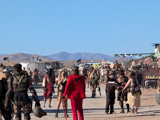 A street crowd including someone in a bright red suit among the leather and armor.