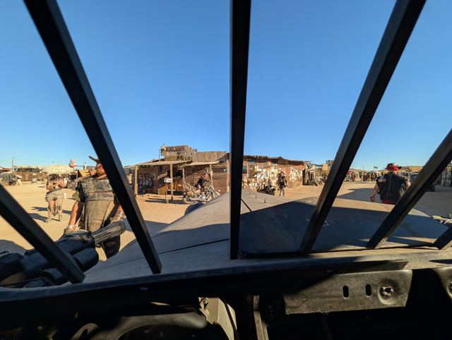 View through the war car's barred window frame onto the dusty street.