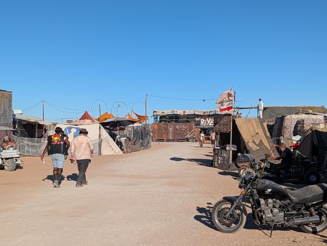A shack-lined lane with a motorcycle parked by a canvas stall.