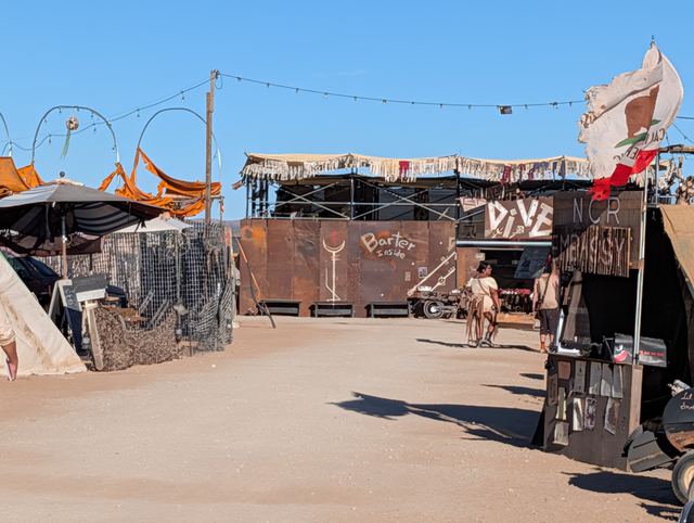A hand-built frontage with rusted metal and flags, laundry lines overhead.