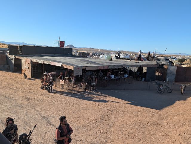 A low shade-covered market building with wastelanders out front.