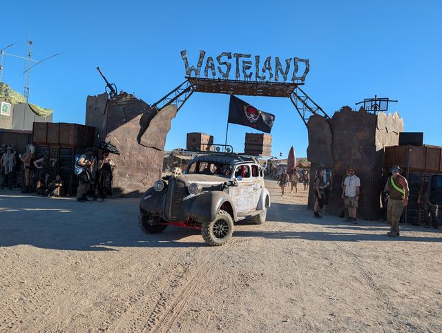 The war car rolls under the gate flying its black tribal flag.