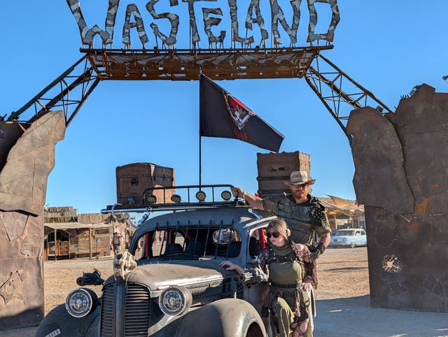 The war car close up under the Wasteland sign, crew climbing aboard.