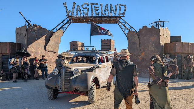 The war car under the Wasteland gate with walkers passing by.