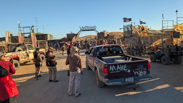 A pickup with painted slogans drives toward the gate past walkers.